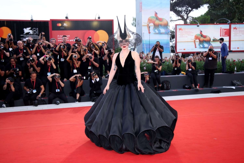 Lady Gaga appeared at Venice Film Festival wearing a giant black ballgown with a petal-like hoop skirt and a plunging neckline along with a towering black lace headpiece. The event marked her red carpet debut with fiancé Michael Polansky.