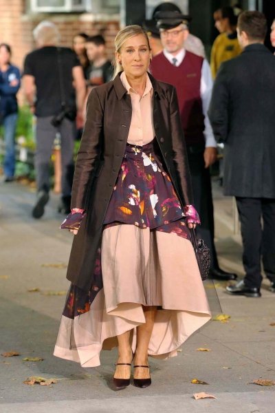 Look of the Day for October 22, 2024 features Sarah Jessica Parker in a chaotic, layered outfit including a puffy maxi dress, brown satin coat, and brown Mary Jane mules while out in New York City.