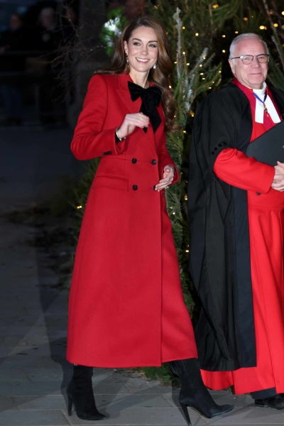 Kate Middleton arrived at her annual Christmas Carol concert wearing a floor length red pea coat that feature a large, black velvet bow at the neckline. She accessorized with velvet black boots.