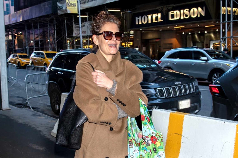 Katie Holmes was spotted in New York City wearing a look that was equal parts chic and practical, pairing a stylish brown maxi wool coat with a Hello Kitty tote bag.